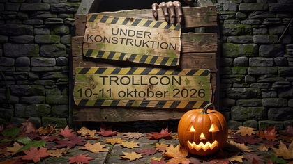 Två träskyltar med text om Trollcon 2026, en pumpa med ljus och höstlöv på marken, stenvägg i bakgrunden.