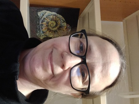 Person i svart tröja framför en bokhylla med en tavla som föreställer ett fossil och ögon.