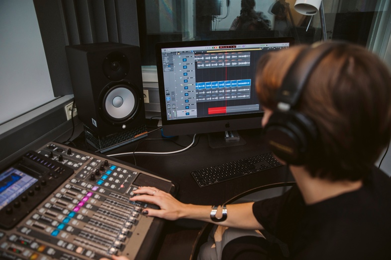 Person med hörlurar arbetar vid ljudmixer och dator i en inspelningsstudio.