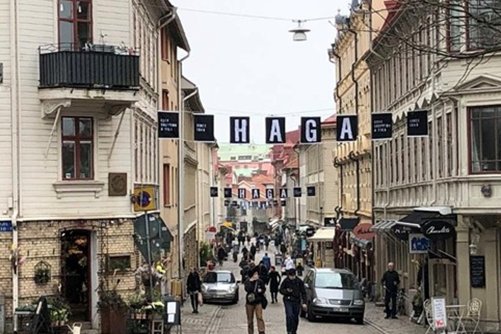 Gata i stadsdelen Haga med gamla trähus, butiker, caféer och människor som promenerar.