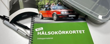 Ett grönt häfte med texten 'Hälsokörkortet', pennor, matlåda, träningsband och broschyr på ett bord.