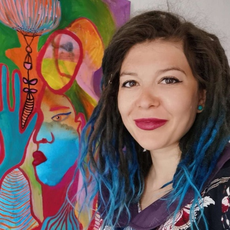 Kvinna med blått hår står bredvid en färgstark abstrakt målning på väggen.