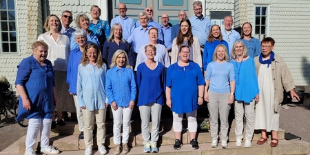 En grupp vuxna står utomhus på trappan framför en byggnad, de flesta klädda i blått och vitt.