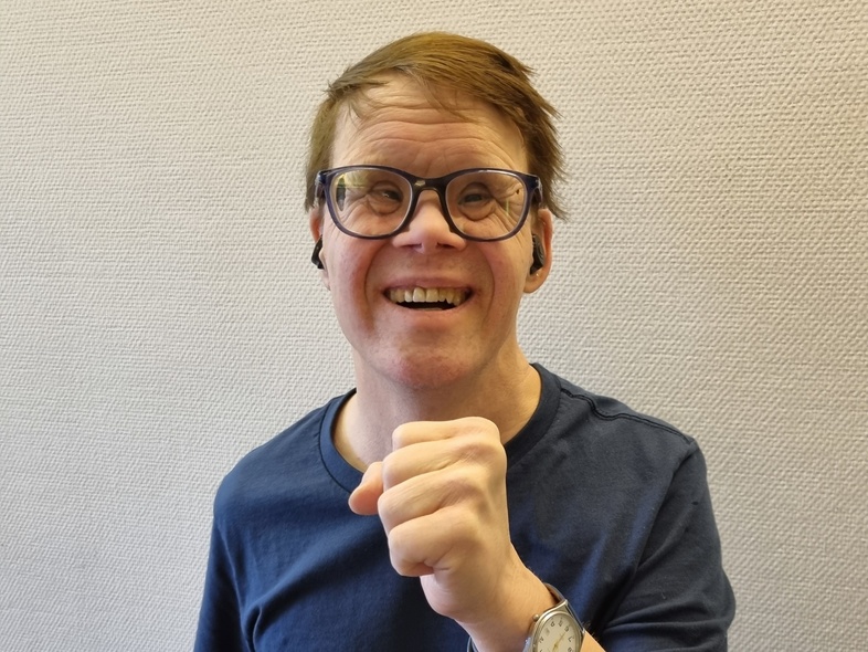 Person i mörkblå t-shirt visar en knuten näve framför bröstet, ansiktet är suddat.