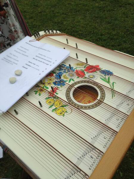 En cittra med blommönster och noter på papper ovanpå, placerad utomhus på gräs.