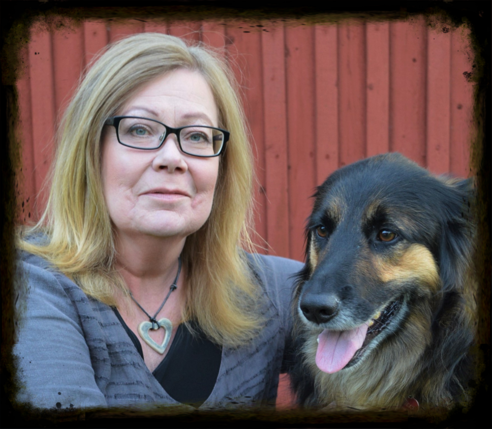 Person med blont hår och grå tröja sitter bredvid en hund framför en röd trävägg.