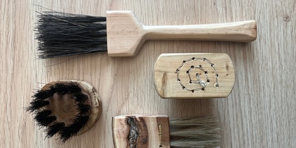 Fyra handgjorda borstar av trä och naturborst ligger på ett ljust trägolv.