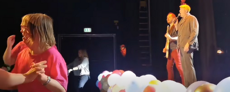 Scenframträdande med musik och dans, ballonger i förgrunden och personer på scen och dansgolv.