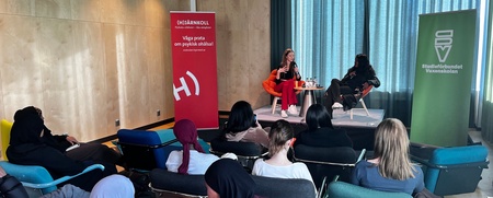 En liten publik lyssnar på två personer som samtalar på en scen i ett modernt konferensrum.