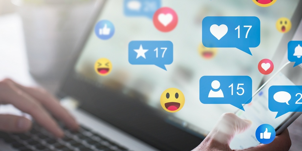 En person använder både en laptop och en smartphone med sociala medie-ikoner och notiser på skärmen.