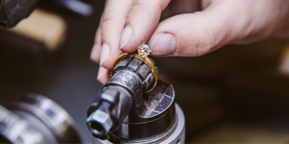 En hand arbetar med att sätta en diamant i en guldring med hjälp av ett verktyg.