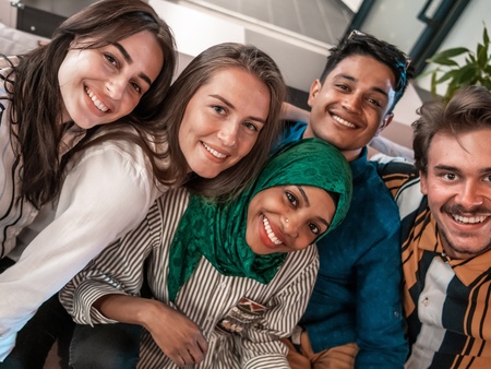 Fem unga vuxna sitter nära varandra i en soffa och ler mot kameran.