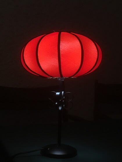 En bordslampa med röd, rund lampskärm som lyser i mörk miljö.