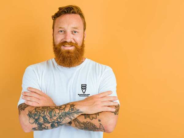 Man med t-shirt med SV-logga står framför en gul vägg.