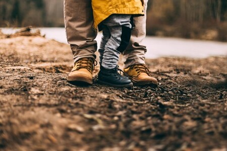 Ett barn och en vuxen står tillsammans utomhus på en jordig stig, endast deras ben och fötter syns.