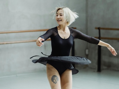 En ballerina med kort blont hår snurrar i en svart dräkt i en dansstudio med ljusa väggar.