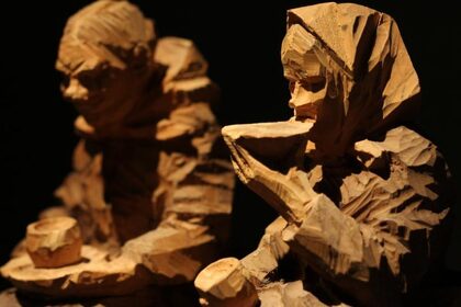Två grovt snidade träfigurer som föreställer personer som dricker och håller koppar.