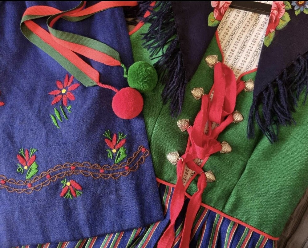 Detaljer från en folkdräkt med broderat förkläde, knytskärp med garnboll och livstycke i blå, gröna och röda toner