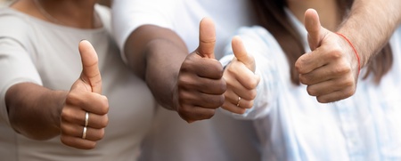 Tre personer visar tummen upp och ler, fokus på händerna och glada ansikten i bakgrunden.