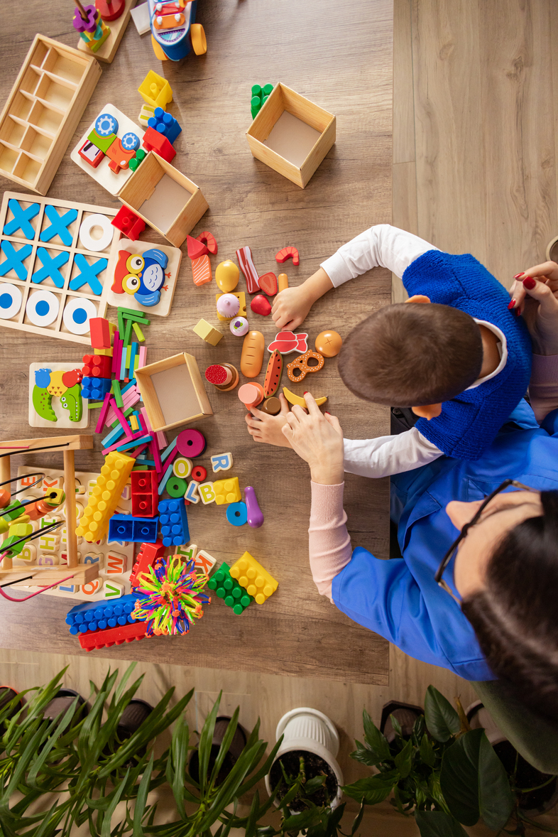 Ett barn och en vuxen leker med färgglada pedagogiska leksaker på ett bord, sedda ovanifrån.