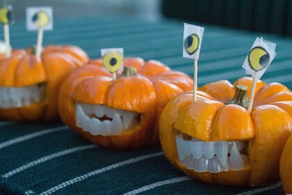 Små pumpor med plasttänder och pappersögon på tandpetare, dekorerade som roliga monster.