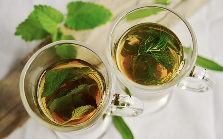 Två glas med örtte, ett med mynta och ett med dill, sedda uppifrån på ett ljust underlag.