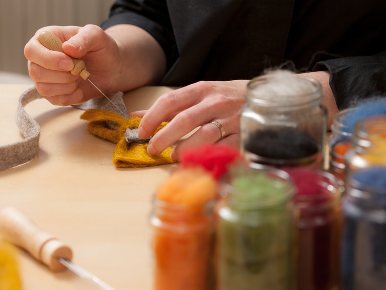 En person arbetar med nåltovning vid ett bord, omgiven av burkar med färgad ull.