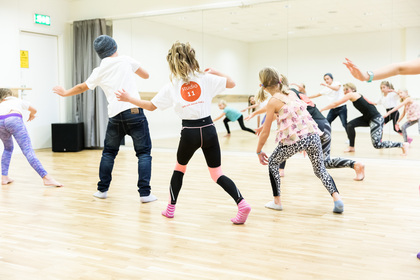 Barn dansar tillsammans i en ljus dansstudio med trägolv och spegelvägg.