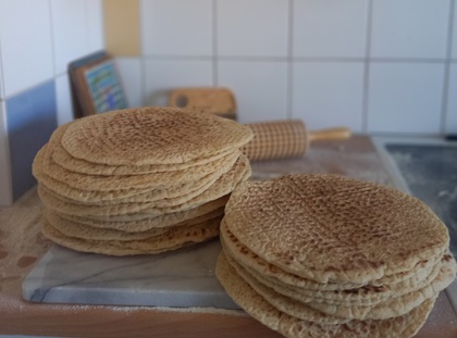 Två högar med runda, platta bröd på en köksbänk med en kruskavel i bakgrunden.