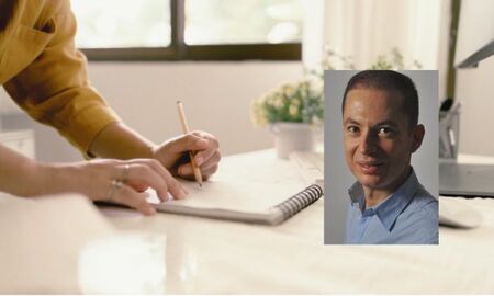 Person skriver i anteckningsbok på ett ljust kontor med växter och fönster i bakgrunden.