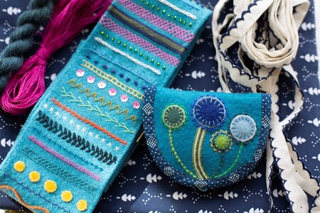 Broderade textilier i blå och turkosa nyanser, inklusive en liten väska och band, på ett mönstrat tyg.