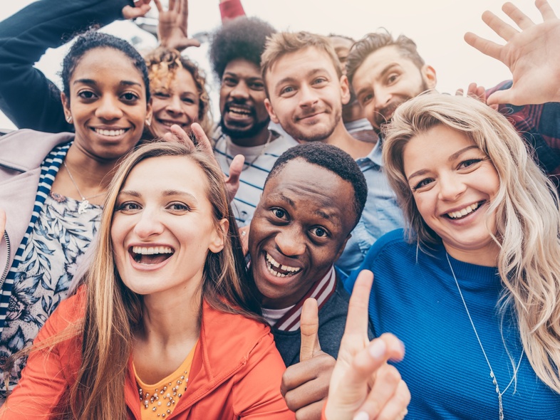 En grupp glada unga vuxna står tätt tillsammans och ler mot kameran utomhus.