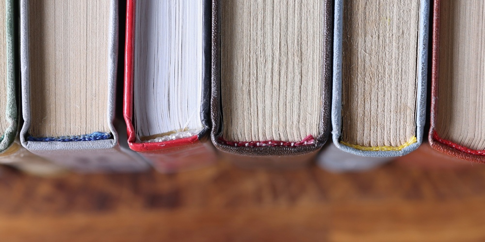 Böcker stående på rad, fotograferade ovanifrån med fokus på bokryggarna och träbordet under.