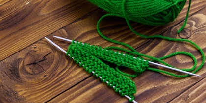 Grönt garnnystan och stickning på träbord med två stickor och påbörjat arbete.