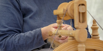 Person spinner garn med en gammaldags spinnrock, fokus på händer och verktyg.