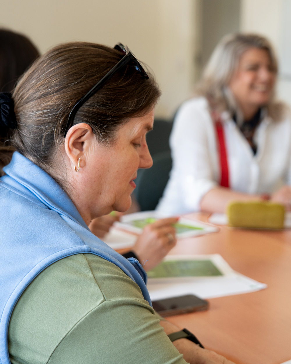 Två kvinnor sitter vid ett bord och deltar i ett möte eller en diskussion.