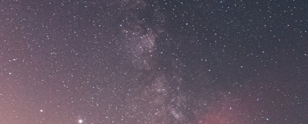 Ett rött fyrtorn lyser under en stjärnklar natthimmel med Vintergatan synlig ovanför.