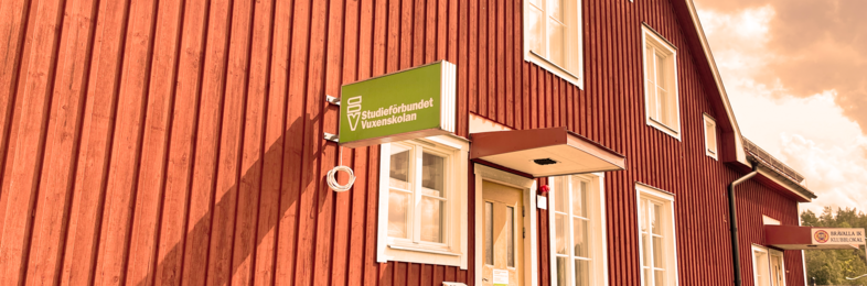 Röd träbyggnad med vita fönster och en grön skylt med texten 'Studieförbundet Vuxenskolan'.