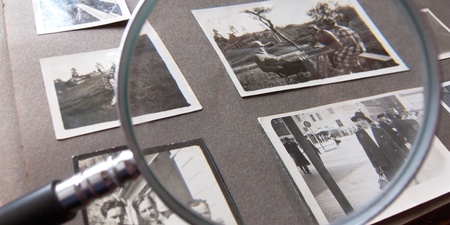 Ett fotoalbum med svartvita fotografier granskas med ett förstoringsglas.