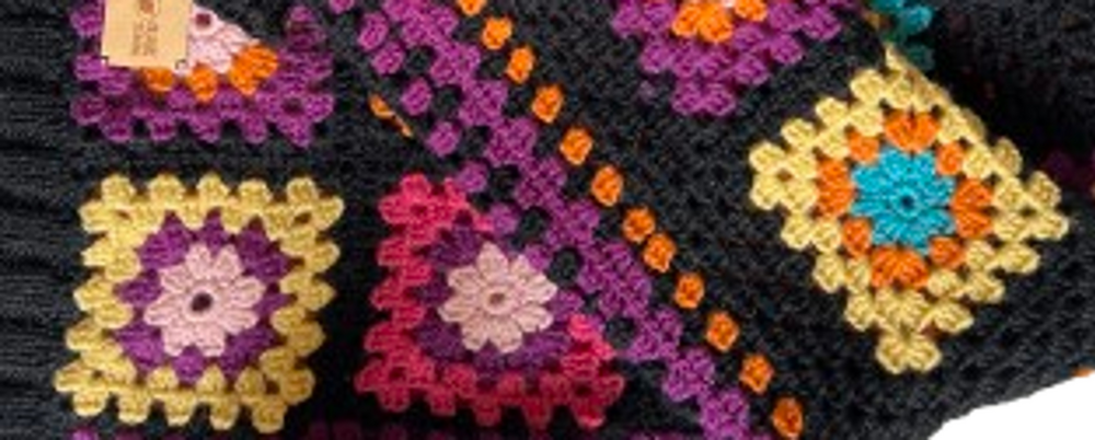 Färgglad virkad filt med mormorsrutor i olika färger på svart bakgrund, vikt på ett bord.