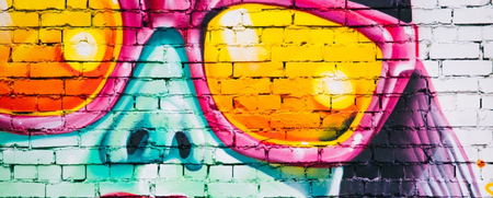 Färgglad graffiti av ett ansikte med stora gula solglasögon på en tegelvägg.