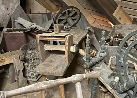 Ett gammalt snickeri med träverktyg, spinnrock och korgar i en dammig vindsmiljö.