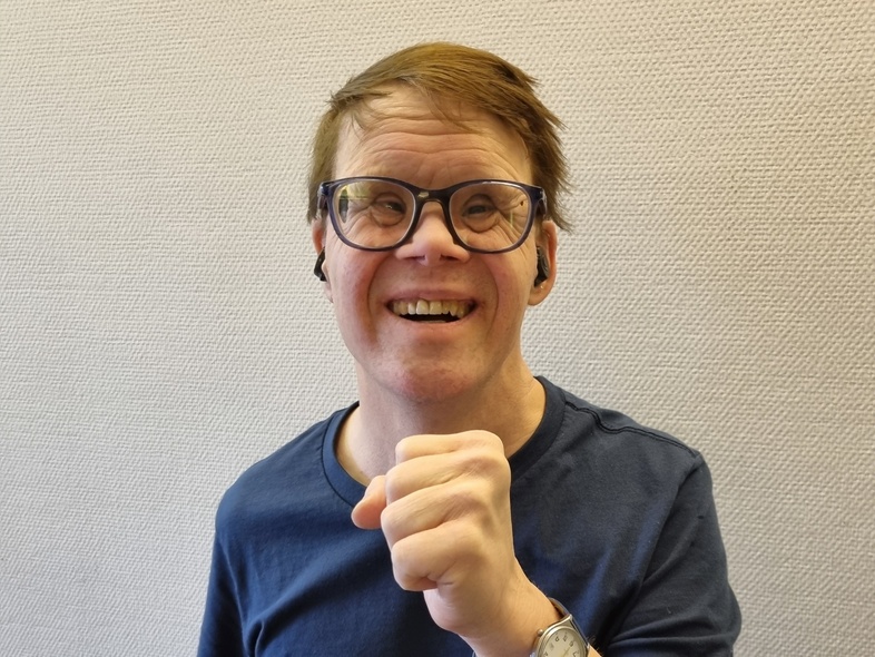 Person i mörkblå t-shirt visar en knuten näve framför bröstet, ansiktet är suddat.