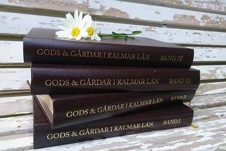 Fyra bruna böcker med titeln 'Gods & Gårdar i Kalmar län' ligger staplade på en sliten träbänk med två prästkragar ovanpå.