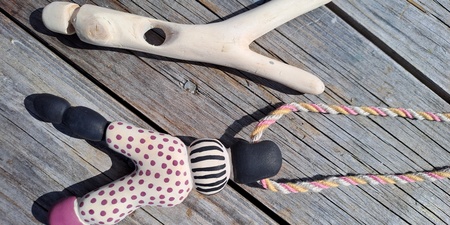 En gammaldags klädnypa i trä och en färgglad docka med snöre ligger på ett trägolv utomhus.