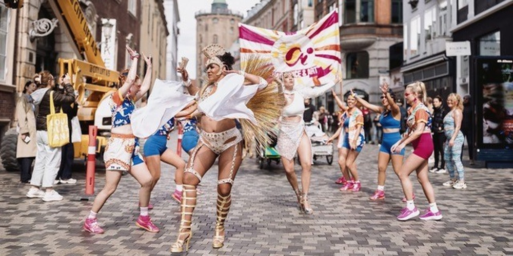 En grupp människor dansar i färgglada kläder på en stadsgata under en festival eller parad.