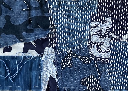 Närbild av ett lapptäcke med blå och vita tyger, synliga stygn och olika mönster.