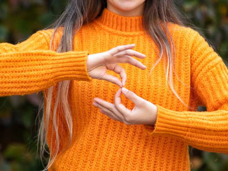 En person i orange polotröja håller händerna framför kroppen i en gest.