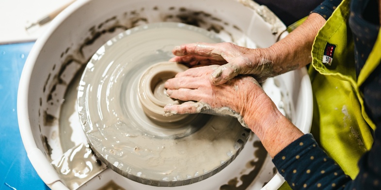 En person formar lera på en drejskiva med händerna, omgiven av vatten och lerskvätt.