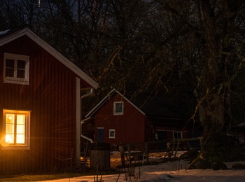 Röd stuga med tända fönster i snöigt landskap under stjärnklar natthimmel.